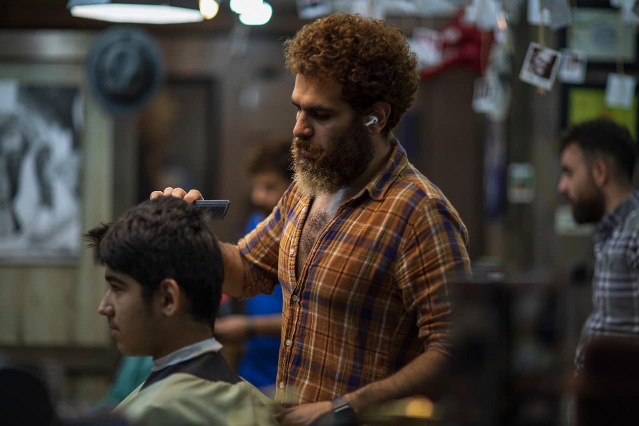 A barber combing through a young customer’s hair before the cut