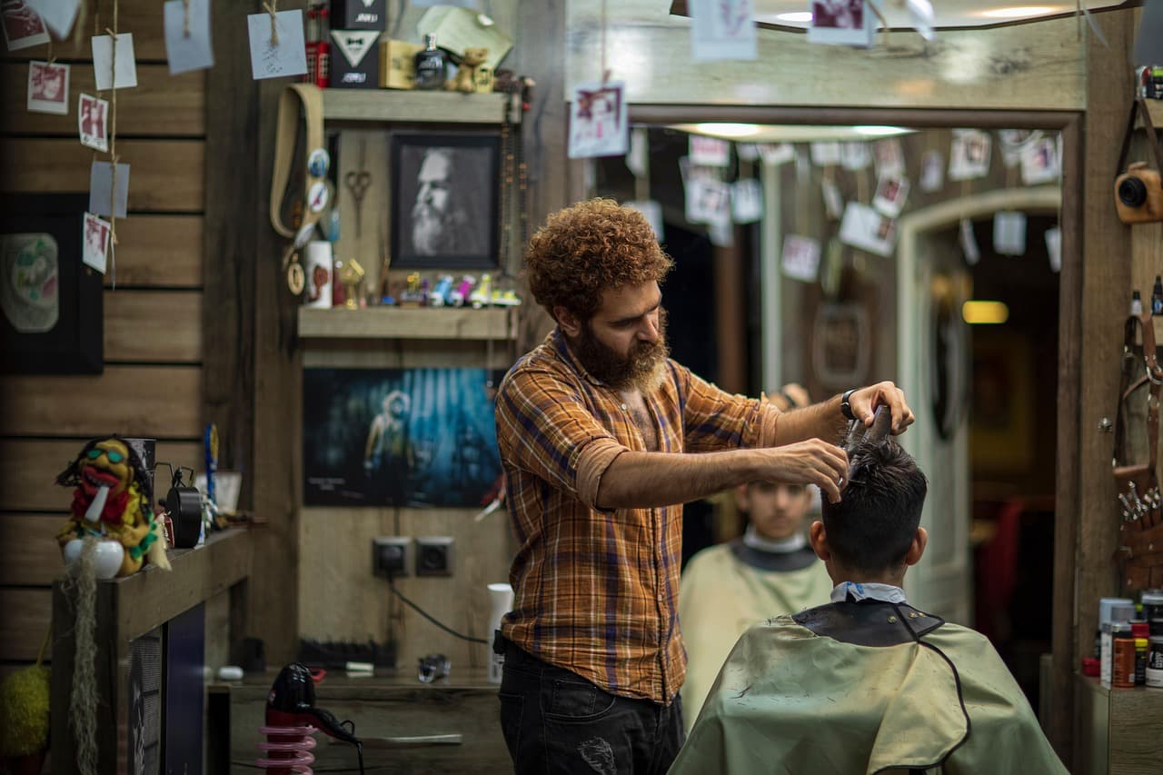 A barber at work in a busy shop lined with mirrors and photos